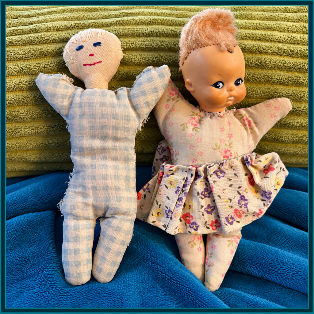 Two well-loved childhood rag dolls, one with a floral body and plastic head, the other with a gingham body and handmade cloth face.